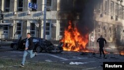 People run to safety as cars burn after a Russian military strike in central Kyiv, Ukraine, Oct. 10, 2022. Multiple explosions rocked Kyiv early Monday following months of relative calm in the Ukrainian capital. 