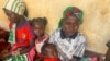 FILE - A woman who fled the violent rebellion in Central African Republic (CAR) sits with her family as they wait for their identification process in the border town of Garoua Boulai, Cameroon, Jan. 7, 2021.