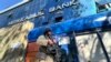 FILE - An armed Taliban guard stands outside a bank, in Kabul, Afghanistan, Feb. 13, 2022.