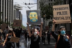 A woman holds a sign showing George Floyd while marching on Market Street at a protest calling for an end to racial injustice and accountability for police in San Francisco, June 20, 2020.