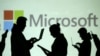 Las siluetas de usuarios de computadoras portátiles y dispositivos móviles se ven junto a una proyección de pantalla del logotipo de Microsoft en esta ilustración.