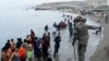 Seorang petugas Spanyol menunjukkan arah yang harus diikuti oleh warga Maroko di pantai El Tarajal, Ceuta, Spanyol, saat mereka keluar dari air di sisi Spanyol pagar perbatasan Spanyol-Maroko, Selasa, 18 Mei 2021. (REUTERS/Jon Nazca)
