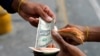 Un hombre cambia un billete de un dólar con el asistente del conductor del autobús, que sostiene un fajo de billetes de Bolívar, en una parada de autobús frente a la estación de metro Antimano en Caracas, Venezuela, el 9 de marzo de 2021.