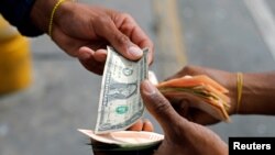 Un hombre cambia un billete de un dólar con el asistente del conductor del autobús, que sostiene un fajo de billetes de Bolívar, en una parada de autobús frente a la estación de metro Antimano en Caracas, Venezuela, el 9 de marzo de 2021.