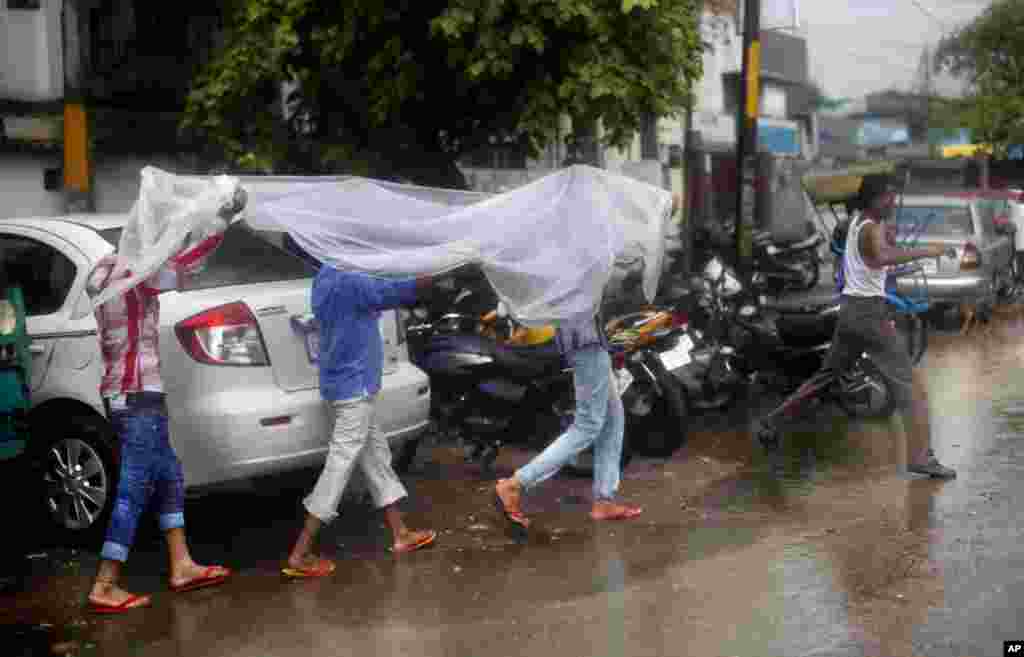 Tiga orang laki-laki India menutupi diri mereka dengan lembaran plastik agar tidak kehujanan di New Delhi, India. Musim hujan yang biasanya turun di India dari bulan Juni hingga September sangat penting bagi para petani di negara itu yang hasil panennya digunakan untuk memenuhi kebutuhan pangan ratusan juta orang.