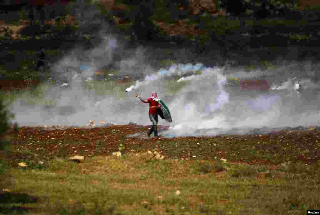 Seorang demonstran Palestina mengembalikan tabung gas air mata ke arah pasukan keamanan Israel selama bentrokan pada Hari Nakba di dekat kota Ramallah, Tepi Barat.