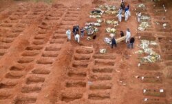 FILE - Cemetery workers in protective clothing bury three victims of the new coronavirus at the Vila Formosa cemetery in Sao Paulo, Brazil, July 15, 2020.