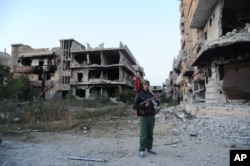 FILE - A civilian fighter holding the Libyan flag stands in front of damaged buildings in Benghazi, Libya, Feb. 23, 2016.