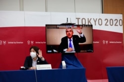 Presiden Komite Olimpiade Internasional (IOC) Thomas Bach (pada layar televisi) dan presiden Tokyo 2020 Seiko Hashimoto (kiri), melambaikan tangan pada awal pertemuan lima pihak di Tokyo, Kamis, 8 Juli 2021. (Behrouz Mehri/Pool Photo via AP)
