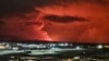 Houses in the village of Hafnarfjordur is seen as smoke is billowing in the distance as the lava colour the night sky orange from an volcanic eruption on the Reykjanes peninsula, western Iceland on December 18, 2023.