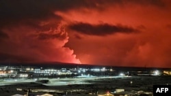 Houses in the village of Hafnarfjordur is seen as smoke is billowing in the distance as the lava colour the night sky orange from an volcanic eruption on the Reykjanes peninsula, western Iceland on December 18, 2023.