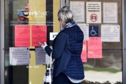 FILE - A woman checks job application information in front of an Illinois Department of Employment Security WorkNet center in Arlington Heights, Ill., April 9, 2020.