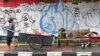 Seorang pemulung menarik gerobak sementara seorang pria tertidur di kursi, Jakarta, 21 April 2020. (Foto: AFP)