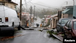 People walk on the street next to debris after the area was hit by Hurricane Maria in Guayama, Puerto Rico, Sept. 20, 2017.