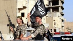 Para pejuang kelompok militan ISIS mengibarkan bendera saat melakukan parade militer di jalan di Suriah utara, 30 Juni 2014. 