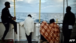 FILE - Migrants look at the coastline as they stand aboard a rescue ship, off the coast of Sicily, May 14, 2018. 