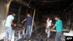 Warga Irak membersihkan kios yang terbakar akibat ledakan dua bom mobil di Baghdad, Rabu (22/7).