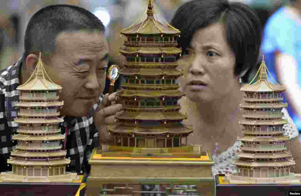 Seorang pengunjung menggunakan kaca pembesar untuk melihat ukiran kayu buatan tangan yang berbentuk sebuah paviliun China kuno di sebuah pameran industri budaya di Taiyuan, provinsi Shanxi, China.